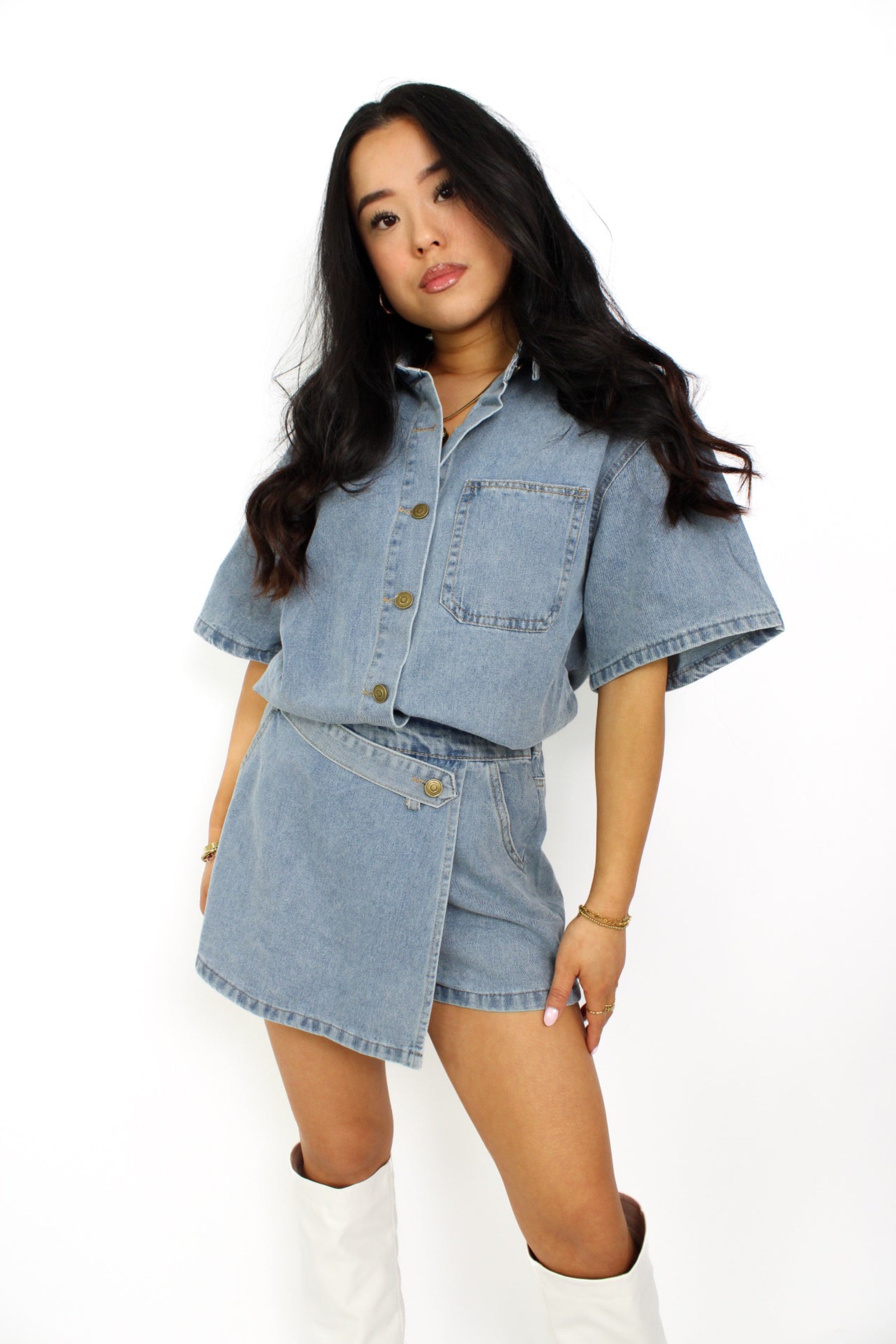 Een trendy denim 2-delig setje bestaande uit een korte top met knoopsluiting en een bijpassende skort. De skort heeft een A-lijn pasvorm met een subtiele rits aan de zijkant en een casual, veelzijdige uitstraling, perfect voor een zomerse look.