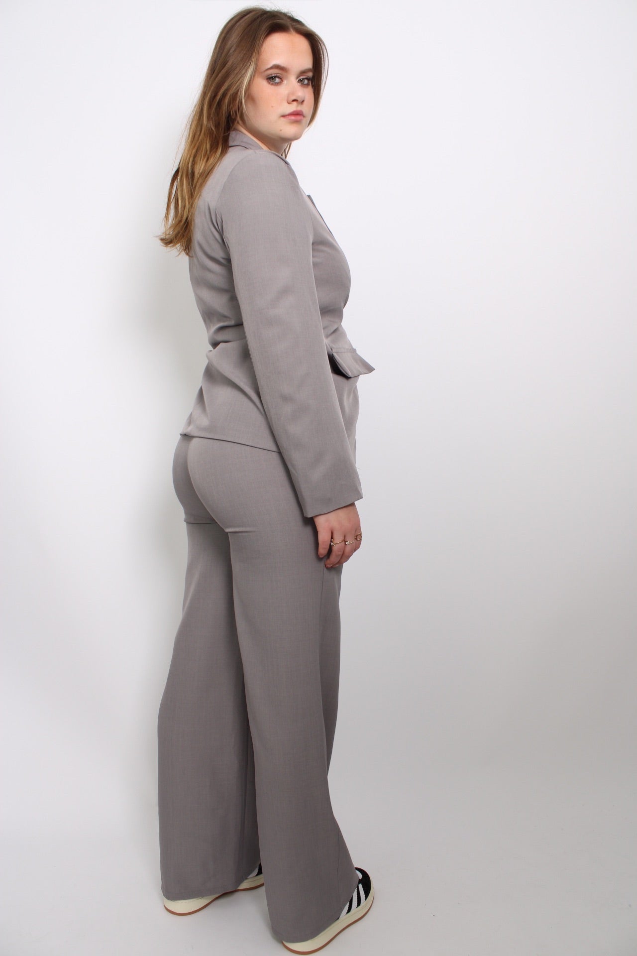 Tweedelige set bestaande uit een grijze pantalon en bijpassende blazer. De pantalon heeft een rechte pasvorm en een klassieke taille, terwijl de blazer een moderne snit heeft met een elegante v-hals en nette afwerking. Beide stukken zijn gemaakt van zacht, rekbaar materiaal voor een comfortabele en stijlvolle look.