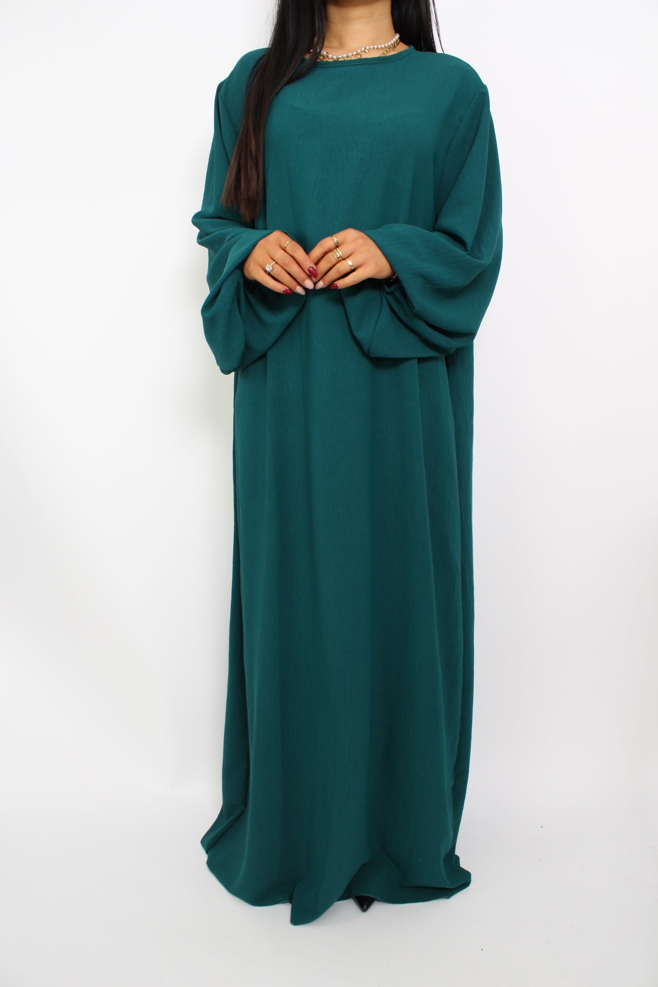 Een basic abaya jurk met een losse pasvorm, lange mouwen en een hoge halslijn. Gemaakt van ademende, niet-doorzichtige stof voor een comfortabele en stijlvolle look."