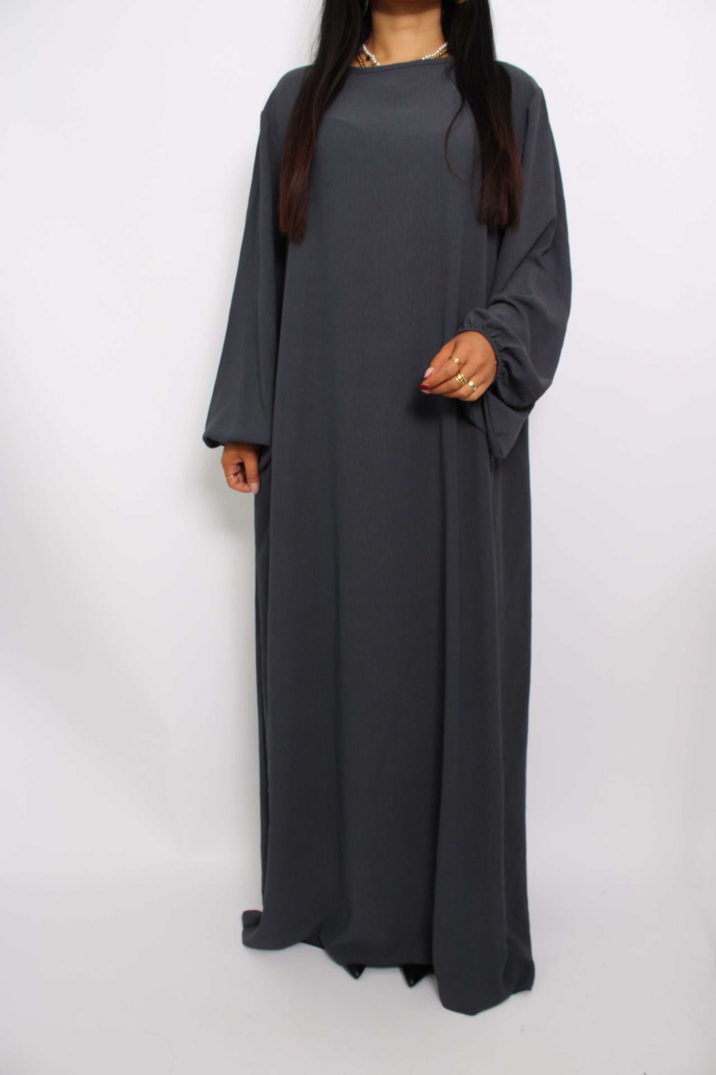 Een basic abaya jurk met een losse pasvorm, lange mouwen en een hoge halslijn. Gemaakt van ademende, niet-doorzichtige stof voor een comfortabele en stijlvolle look."