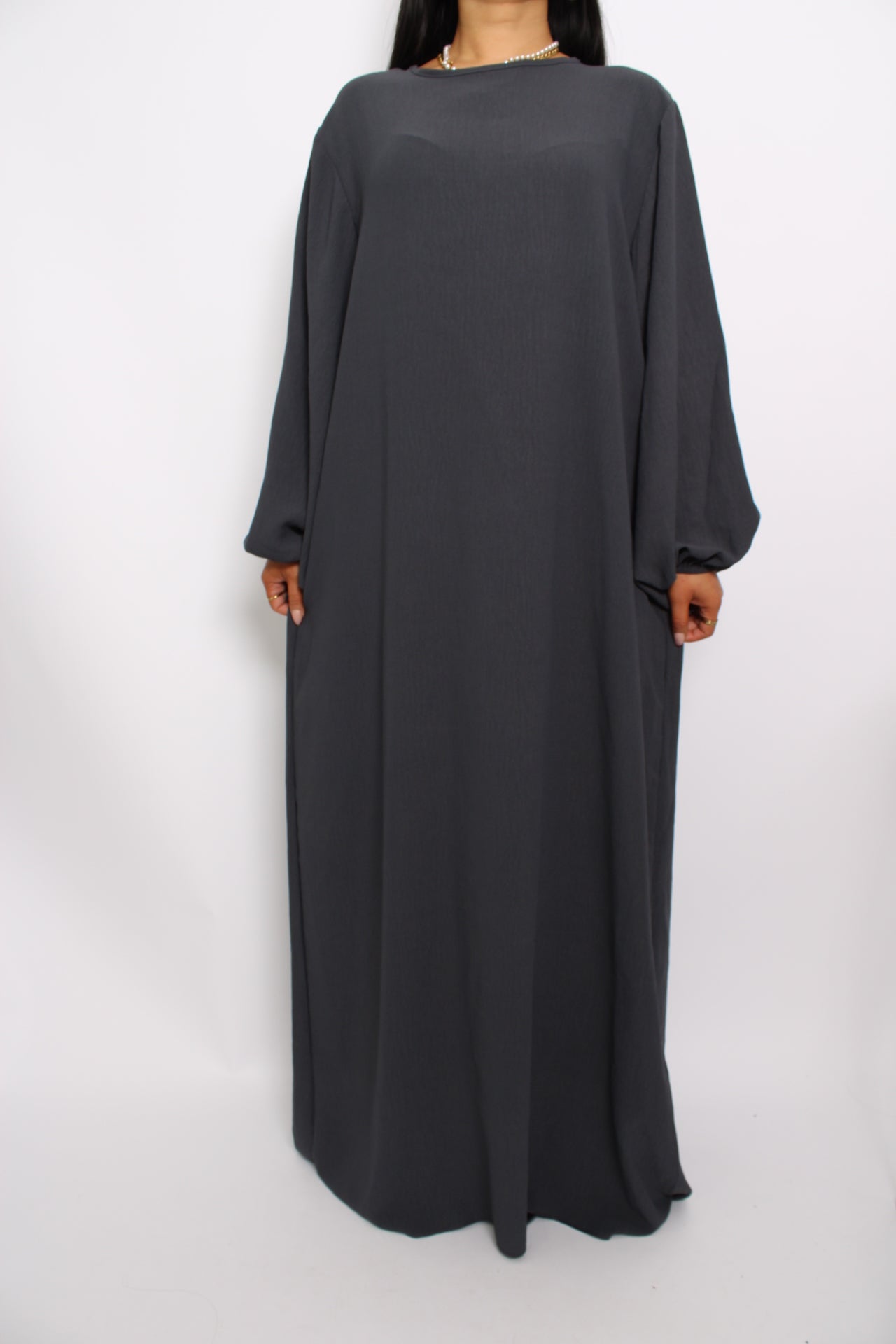 Een basic abaya jurk met een losse pasvorm, lange mouwen en een hoge halslijn. Gemaakt van ademende, niet-doorzichtige stof voor een comfortabele en stijlvolle look."