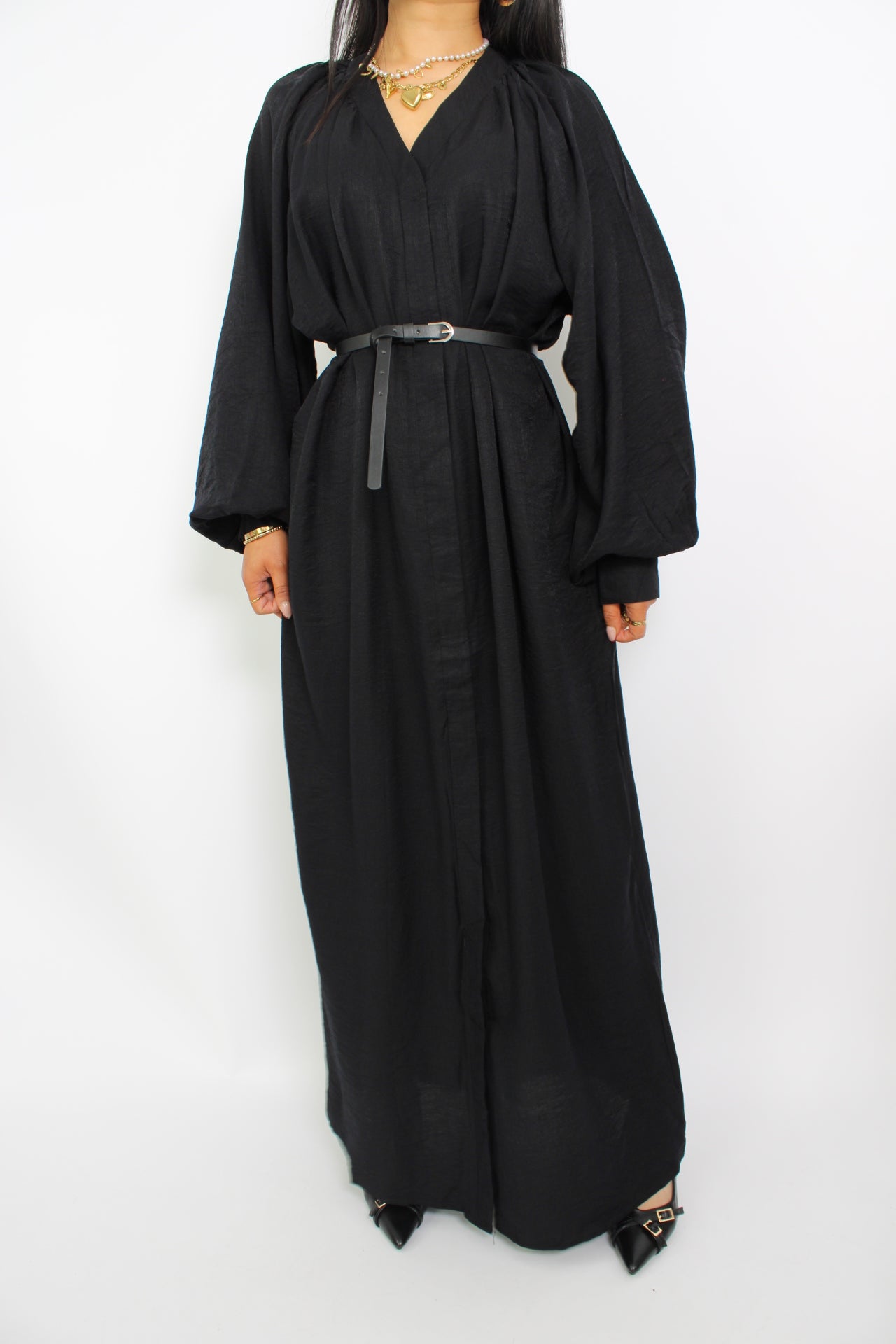 Een modest jurk in zwart, met een losse pasvorm, lange mouwen, een hoge halslijn en een bijpassende ceintuur. Gemaakt van ademende, niet-doorzichtige stof voor comfort en stijl.
