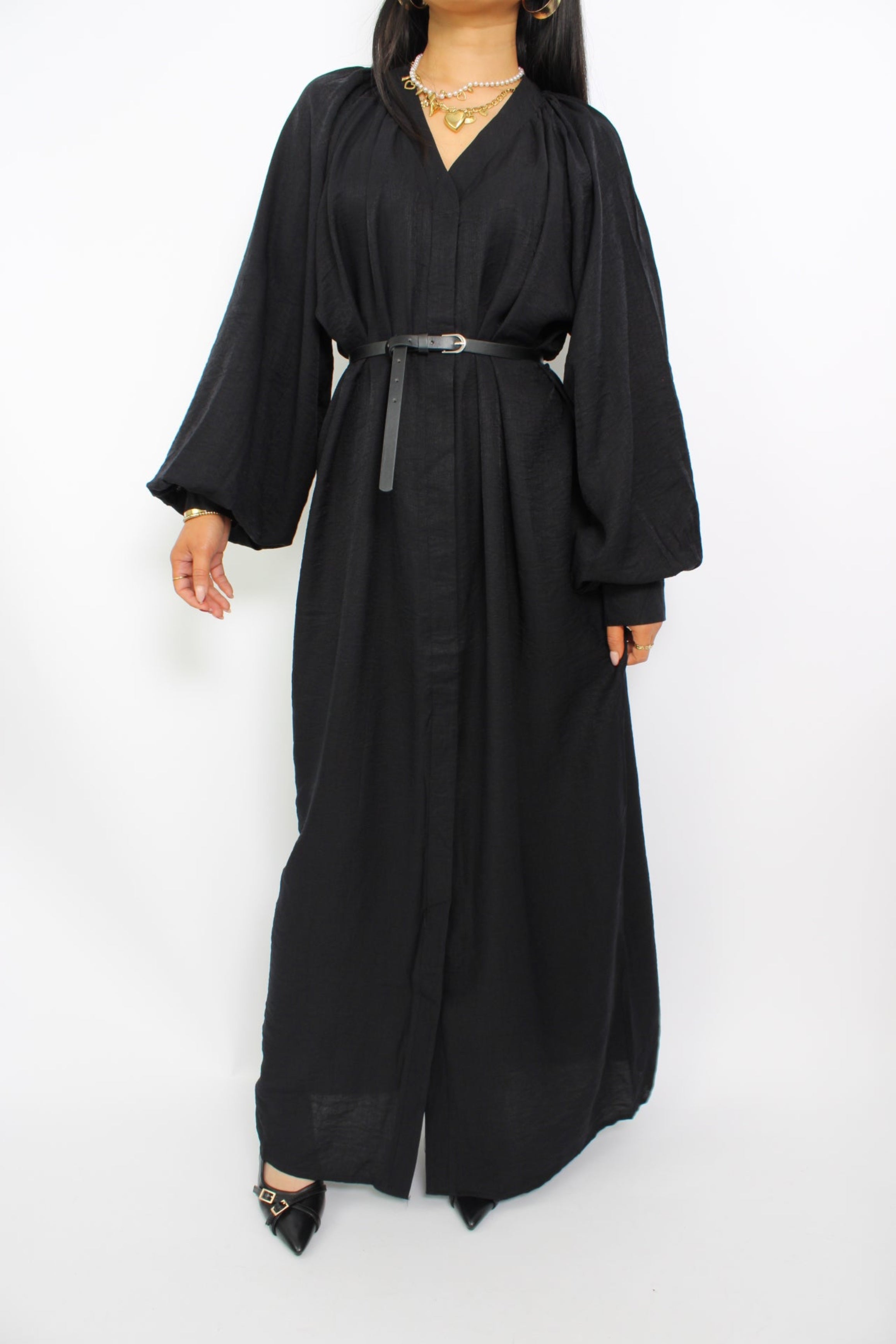 Een modest jurk in zwart, met een losse pasvorm, lange mouwen, een hoge halslijn en een bijpassende ceintuur. Gemaakt van ademende, niet-doorzichtige stof voor comfort en stijl.